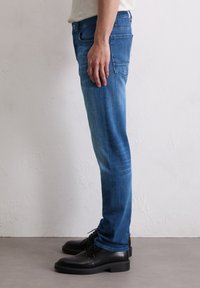 Jeans en denim de couleur bleu clair délavé avec une coupe droite. Comprend cinq poches et une fermeture éclair, associés à des chaussures noires à lacets.