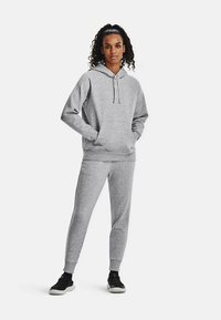 Siva dukserica s kapuljačom s vezicama, kangaroo džepom i rebrastim manžetnama, uparena sa odgovarajućim sivim trenirkama koje imaju suženi kroj i elastični pojas.