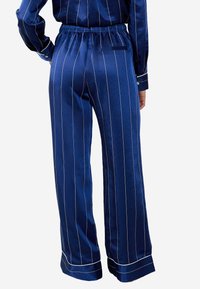 Granatowe satynowe spodnie z białymi pionowymi paskami, elastycznym paskiem w talii i tylną kieszenią. Szerokie, lekko opadające nogawki, gładka tekstura.
