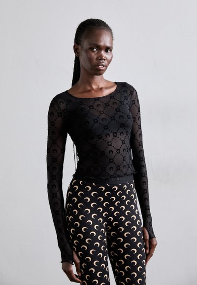 Sort langærmet top med en gennemsigtig, tekstureret stof med blomster mønstre, parret med højtaljede leggings med et halvmåne design.