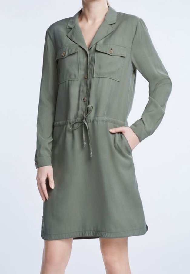 Femme portant une robe-chemise olive verte, mi-longue, à manches longues, avec des poches poitrine boutonnées et une taille à cordon de serrage.