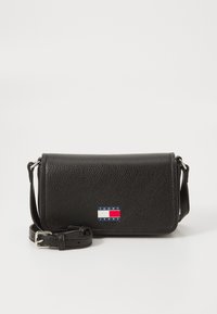 Svart skinn crossover-veske med teksturert overflate, med magnetisk klaffelukk og en markant "TOMMY JEANS" logo i rødt, hvitt og blått.