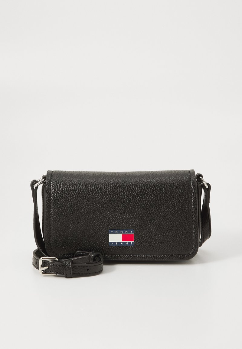 Svart skinn crossover-veske med teksturert overflate, med magnetisk klaffelukk og en markant "TOMMY JEANS" logo i rødt, hvitt og blått.