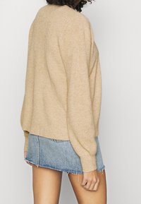 Beige ribbat stickad tröja med långa ärmar. Kombinerad med en ljusblå denimminikjol med fransar och fickor.