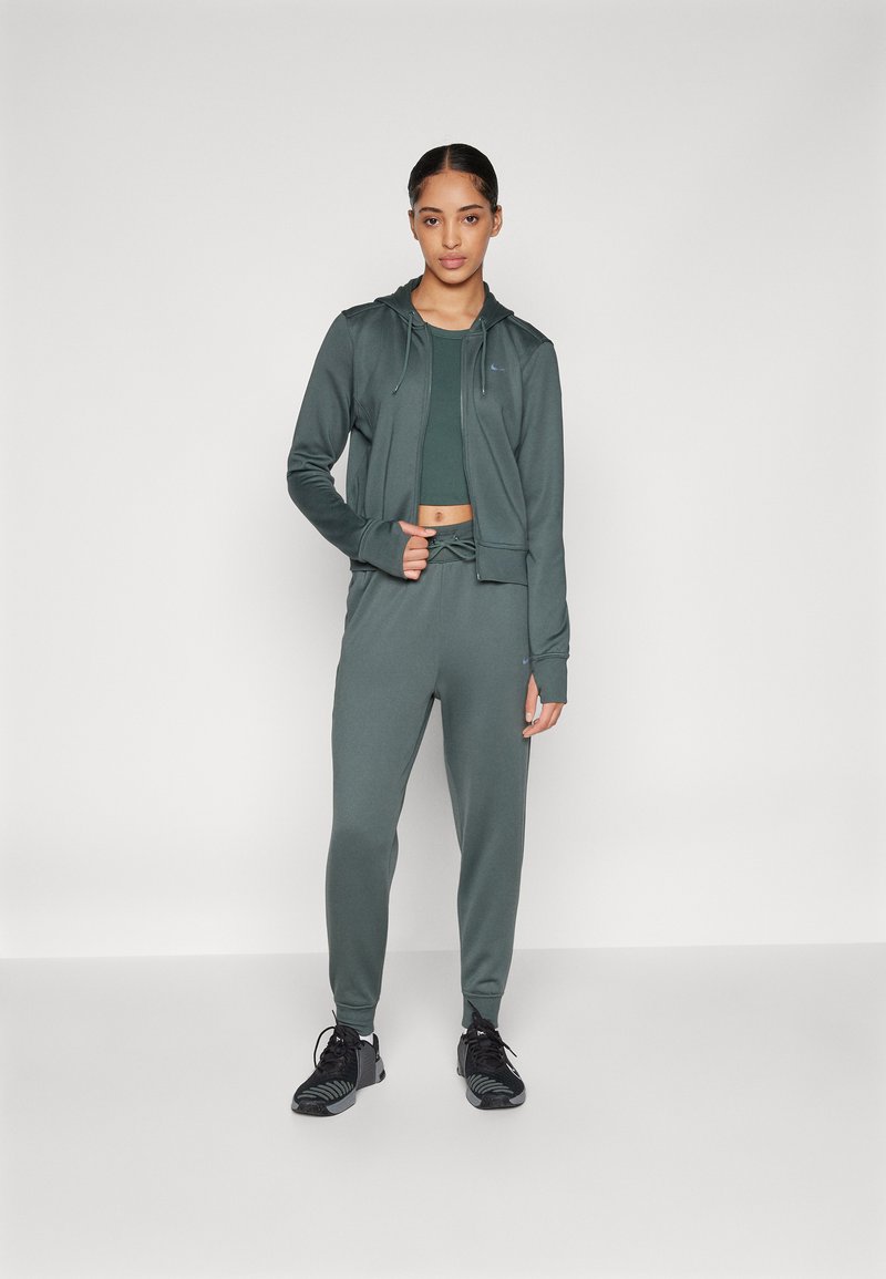 Grünes Sportoutfit, bestehend aus einem eng anliegenden Crop-Top, einem Reißverschluss-Hoodie und engen Hosen, die alle aus einem glatten, dehnbaren Material gefertigt sind.