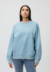 Felpa azzurra con maniche lunghe e scollatura rotonda. Presenta la scritta 'LEGER' in bianco sul petto. Tessuto morbido con un fit rilassato.