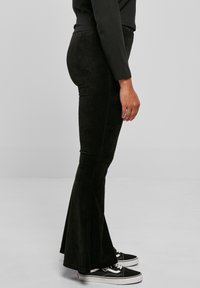 Svarta kordflortbyxor med mjuk textur, åtsittande vid låret och som vidgar sig vid fållen. Tillsammans med svarta kanvas skor.