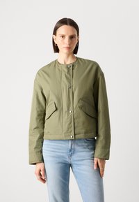 Giacca verde oliva con scollo rotondo, chiusure a pressione e due tasche frontali; presenta una texture liscia e opaca e una vestibilità morbida.