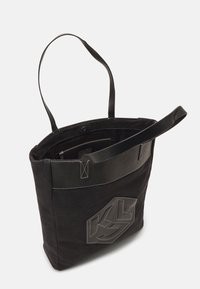 Bolsa tote negra hecha de material de fieltro con acentos de cuero. Presenta un logotipo prominente, diseño cosido y un único asa para llevar.