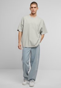 Lys grå oversized t-skjorte i bomull, korte ermer og rund hals, kombinert med lyseblå vide jeans og hvite sneakers.