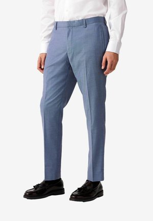 Pantalones ajustados de color azul claro con una textura suave, que presentan un frente plano, bolsillos laterales y líneas de pliegue sutiles, combinados con zapatos negros.