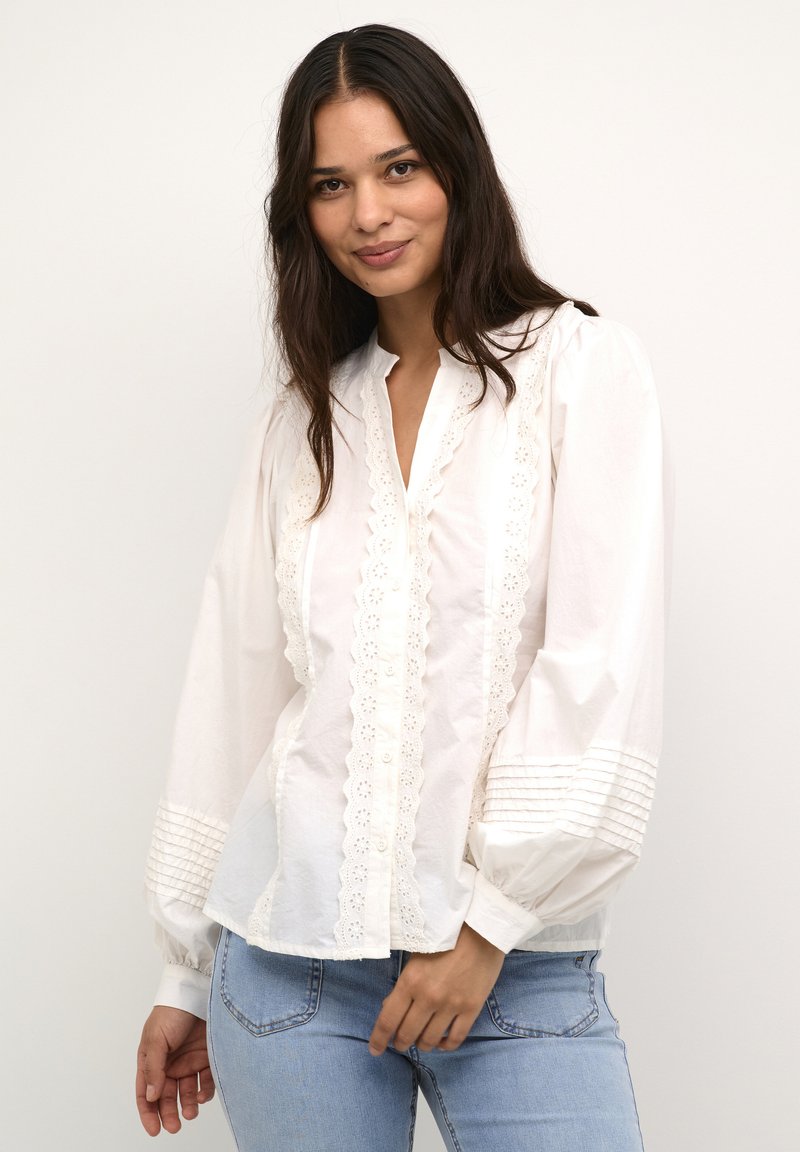 Weiße Bluse mit langen Ärmeln, bestickt, mit Knopfleiste und gerafften Manschetten. Hat einen lässigen Schnitt und einen strukturierten Stoff.