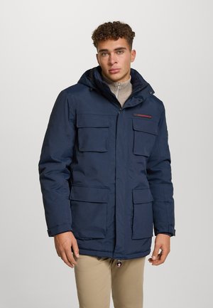 Marineblaue Parkajacke mit Kapuze, fünf Außentaschen, Reißverschluss vorne und roten Logoakzenten. Hergestellt aus strapazierfähigem Material mit strukturierter Oberfläche.
