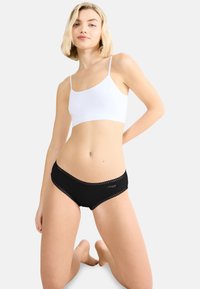 Sort undertøj med blondekant kombineret med en hvid crop top med tynde stropper. Glat stof med en tætsiddende pasform og mellemhøjt talje.