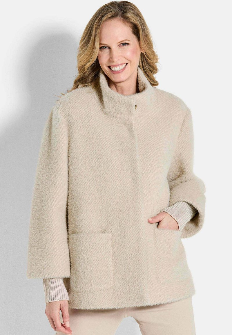 Beige, textuurjasje met een hoge kraag, voorzakken en een ontspannen pasvorm. Heeft geribbelde mouwkappen voor extra detail.