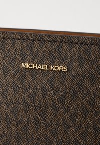 Brązowy portfel z fakturowanej sztucznej skóry z jasnobrązowym tłoczonym wzorem, z złotą płytką logo "MICHAEL KORS" z przodu.