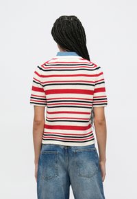 Πλεκτό πουλόβερ με κοντά μανίκια που διαθέτει ρίγες σε κόκκινο, λευκό και ναυτικό μπλε με γιακά. Συνδυασμένο με ψηλόμεσο τζιν παντελόνι σε μπλε χρώμα.