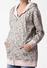 Felpa con zip a motivo floreale in verde e rosa. Presenta una texture morbida, tasche frontali e polsini e orlo a costine. Leggera e dotata di cappuccio.