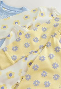 Gestapelte Baby-Pyjamas mit gelben und blauen Blumenmustern auf cremefarbenem, gelbem und hellblauem Stoff aus weichem Baumwollmaterial.