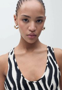 Zwart-wit gestreepte tanktop met een diepe halslijn. Gladde textuur met smalle schouderbandjes. Grote gouden oorbellen met een hoepel.