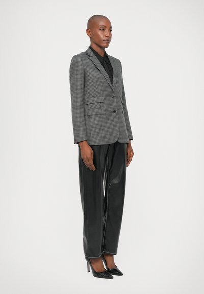 Blazer de patrón de espiga gris con solapas de muesca, cierre de botón y dos bolsillos frontales, combinado con pantalones de cuero negros de cintura alta.