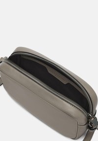 Grijze leren schoudertas met een ritssluiting, voorzien van een gladde textuur en een minimalistisch ontwerp. Het interieur is van donkere stof. Verstelbare schouderband.