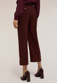 Bordeaux wijde broek met omslagonderkant, voorzien van achterzakken en een gladde textuur, gecombineerd met glanzende hakken.