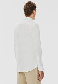 Biała koszula z długim rękawem, wykonana z lekkiego materiału, z klasycznym kołnierzykiem i zapięciami na guziki, z prostym wykończeniem i minimalistycznym wzornictwem.