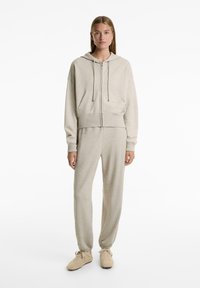 Beige hoodie and matching sweatpants set made of soft material. Hoodie features a zipper, drawstring, and front pockets. Relaxed fit.