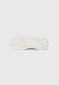 Weiße Sneaker-Sohle mit strukturiertem Design, Rillen und einem Logo. Das Material ist Gummi mit einer glatten Oberfläche und erhabenen Mustern.