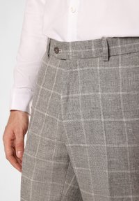 Grau karierte Hose aus einem strukturierten Stoff, mit einem Knopfverschluss und seitlichen Taschen, kombiniert mit einem weißen Langarmhemd.