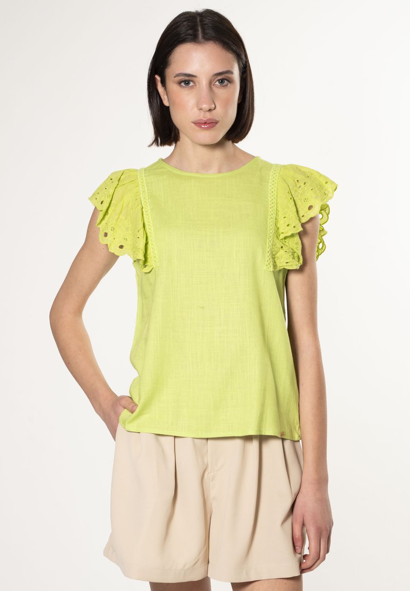Top corto de color verde lima con mangas de volantes de ojales, tejido texturizado y un corte relajado, combinado con pantalones cortos beige claros.