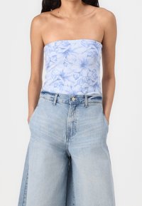 Jasnoniebieski top na ramiączkach z kwiatowym wzorem, w połączeniu z wysokimi, szerokimi dżinsami w jasnym kolorze, z zapięciem na guzik i kieszeniami.