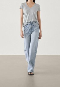 T-shirt grigia a collo a V, jeans a gamba larga blu chiaro e ciabatte nere. Tessuto morbido, vestibilità comoda, con un design semplice e dettagli minimi.