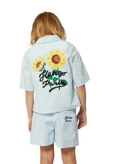 Une chemise à manches courtes bleu clair et un short assorti présentent des tournesols brodés et "Henzo Paris" en écriture noire au dos.