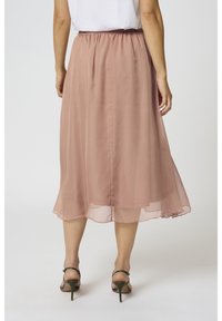 Ljusrosa chiffong midi kjol med resårmidja, mjuk textur och en svajig silhuett, kombinerad med sandaler med remmar och hög klack.