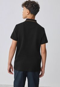 Sort polo skjorte med korte ærmer, prydet med en orange kant på kraven og ærmeenderne, lavet af fleksibelt bomuldsstof.