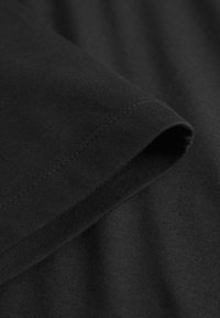 Gros plan sur un tissu noir plié au niveau d'une couture, montrant des points de couture fins et une texture lisse sur la manche d'un vêtement.