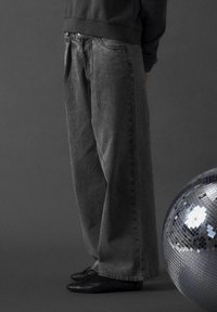 Grå denimjeans med vida ben och mjuk textur, med en klassisk design med fem fickor. I kombination med svarta ballerinaskor.