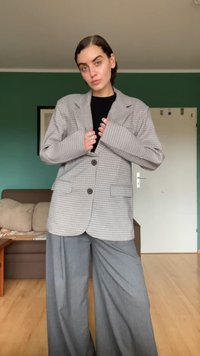 Checks-patterned blazer in light brown and white, with two front buttons, large lapels, and side pockets paired with wide-leg gray trousers.