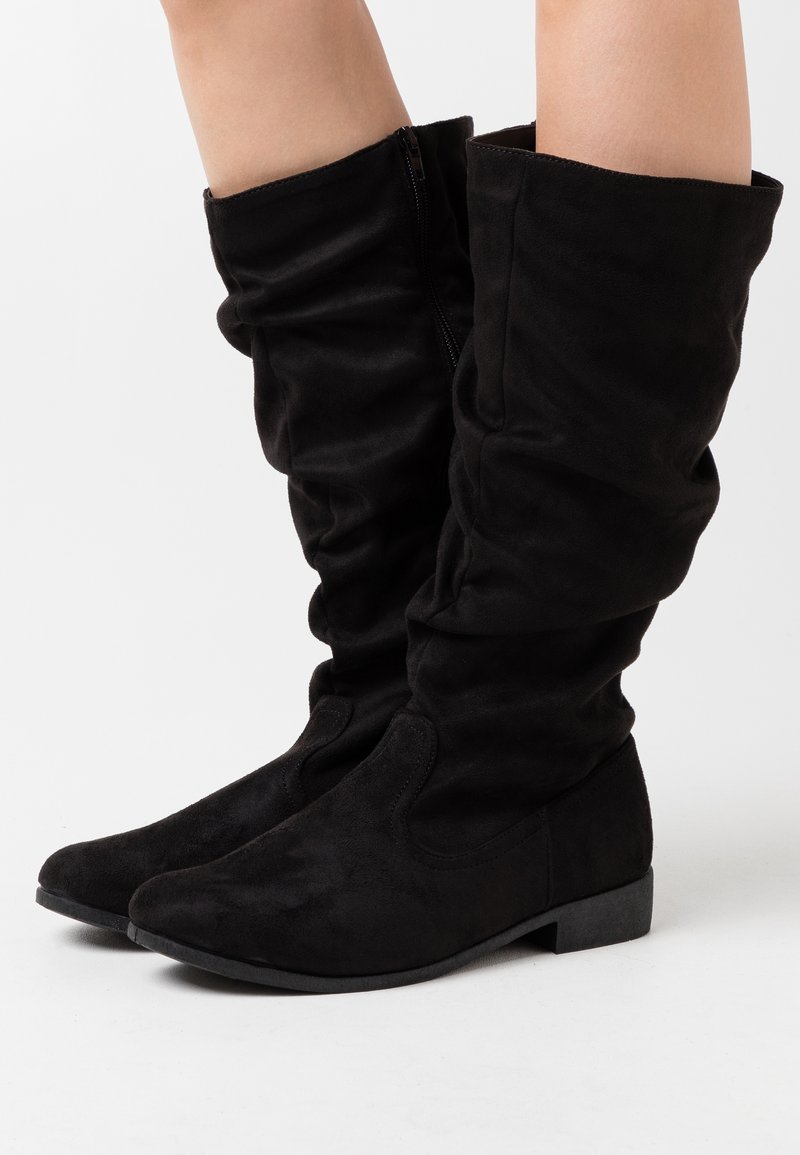 Des bottes noires en daim montantes présentent un design décontracté, un bout arrondi, un petit talon et une fermeture éclair sur le côté pour un enfilage facile. La texture lisse rehausse leur apparence.
