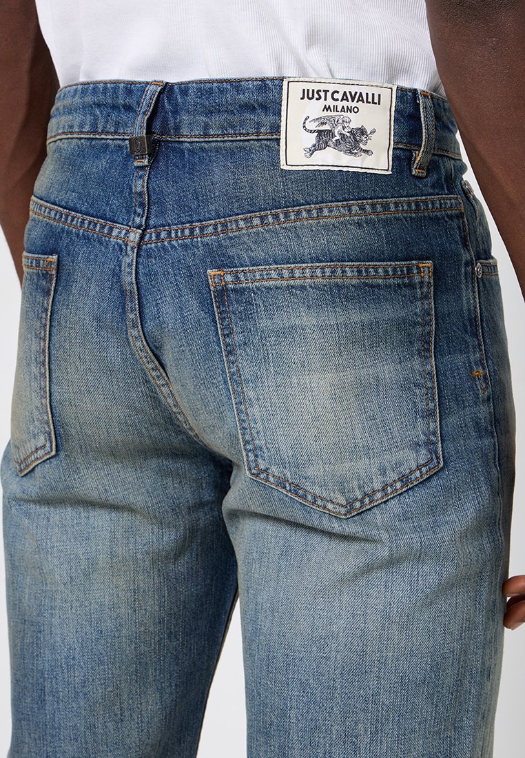 Jean en denim de couleur bleu clair. Dispose de cinq poches, de surpiqures contrastantes et d'une étiquette blanche avec un graphique noir au dos de la taille.