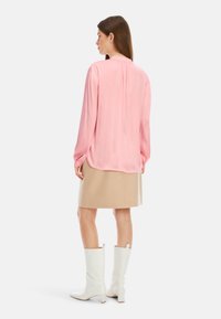 Langärmlige rosa Bluse mit gefaltetem Rücken, kombiniert mit einem beigen Rock und weißen knielangen Stiefeln, die eine glatte Textur und eine maßgeschneiderte Passform aufweisen.