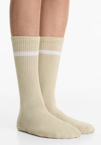 Beige geribde sokken met een witte strepen aan de bovenkant, halverwege de kuit lengte, met een gladde textuur en een klassiek atletisch ontwerp.