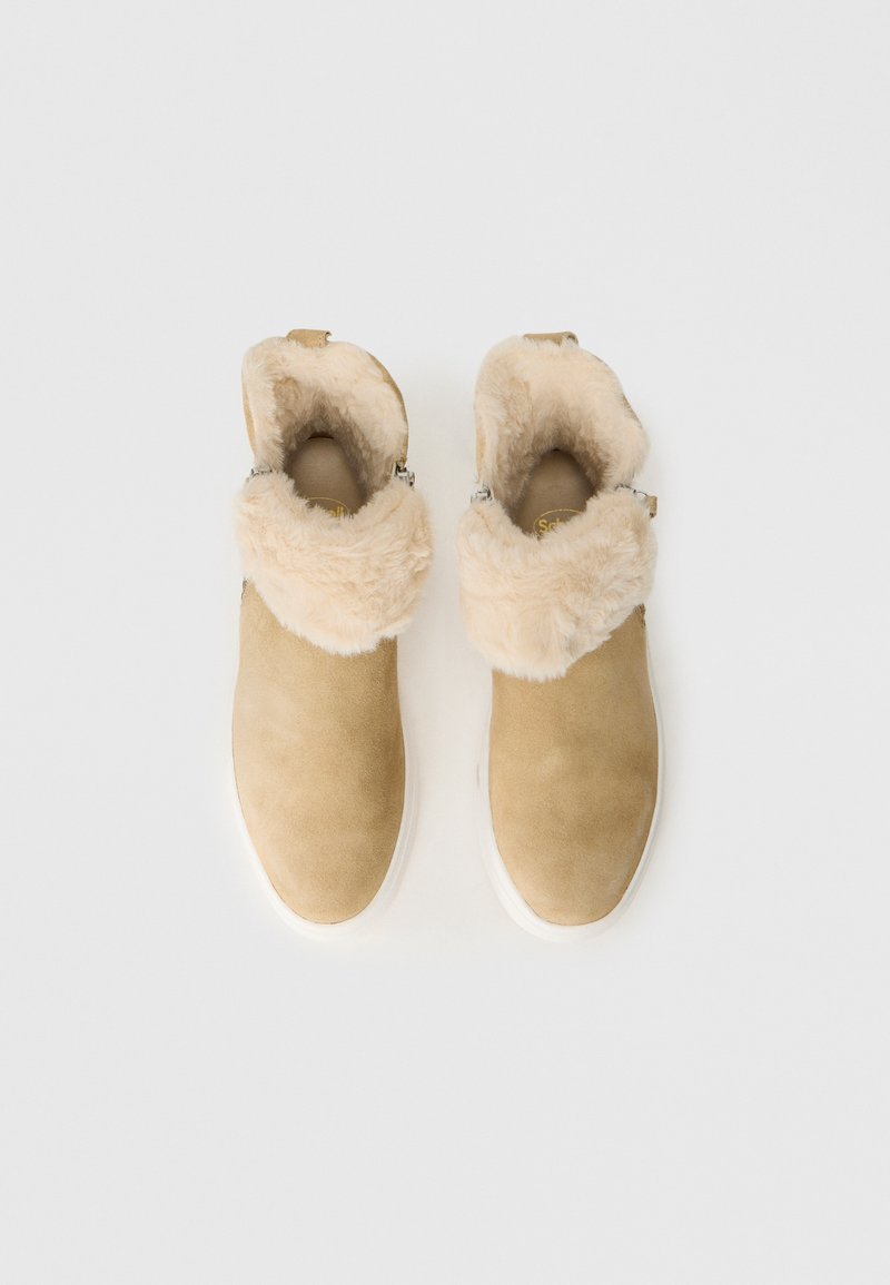 Bruna mockaskinn ankelstövlar med fluffig beige foder, rund tå och vit gummisula. Sidodragkedjedetaljer lägger till funktionalitet.