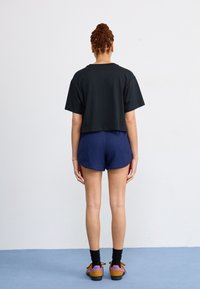 Black cropped t-shirt, ribbed navy shorts, black socks, brown shoes with orange and purple accents. Simple design with relaxed fit.