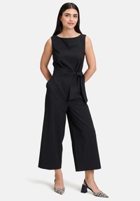 Fekete, ujjatlan overall, testhez simuló felsőrésszel és bő szárú nadrággal, övvel a derékrészen. Texturált anyag, minimalista dizájn, minta nélkül.
