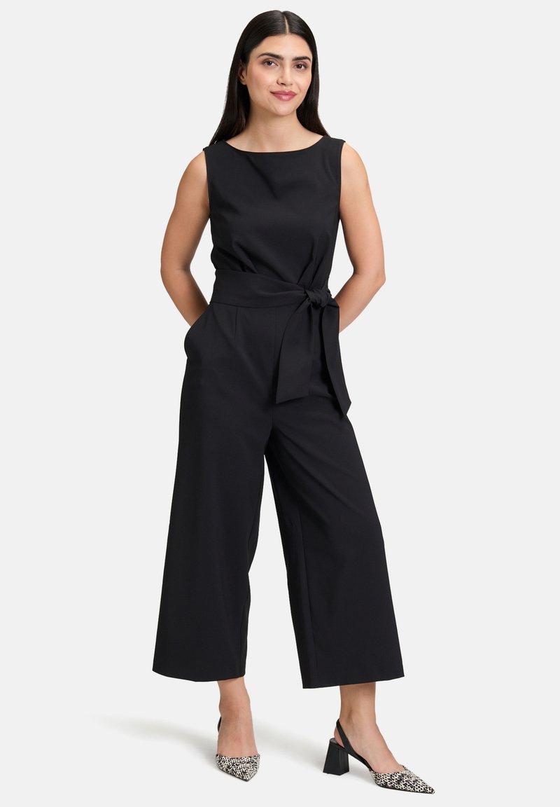 Fekete, ujjatlan overall, testhez simuló felsőrésszel és bő szárú nadrággal, övvel a derékrészen. Texturált anyag, minimalista dizájn, minta nélkül.