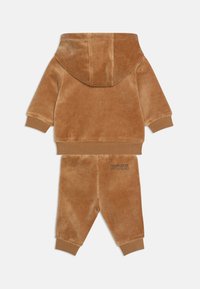 Completo tuta in velluto marrone composto da giacca con cappuccio e pantaloni abbinati. I pantaloni presentano il logo 'BOSS' ricamato in una tonalità più scura.