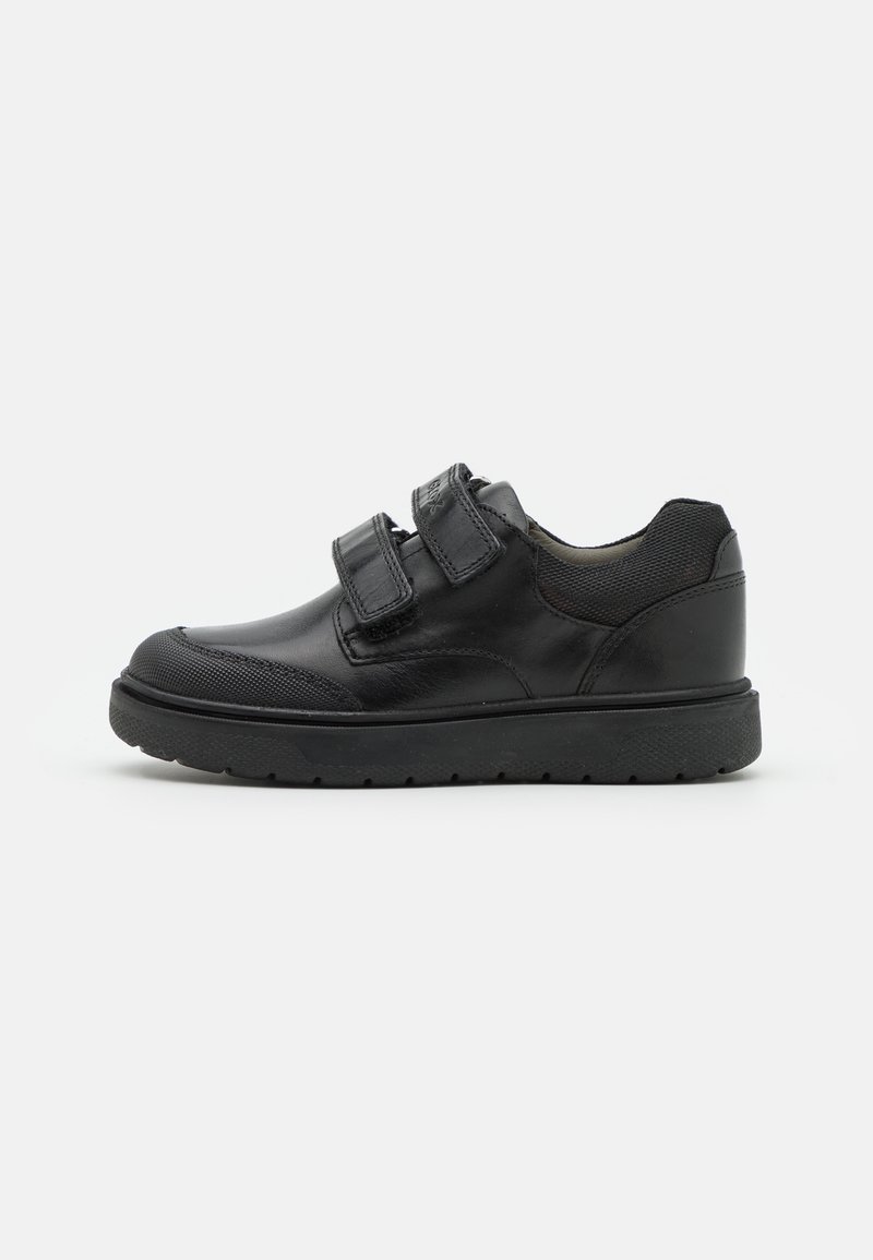 Chaussure décontractée en cuir noir avec deux bandes Velcro, zones texturées au niveau des orteils et du talon, et semelle épaisse en caoutchouc noir.